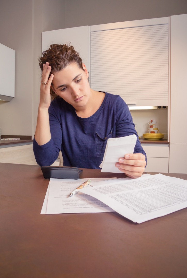 Femme sans emploi et divorcée avec de nombreuses dettes examinant ses factures mensuelles.