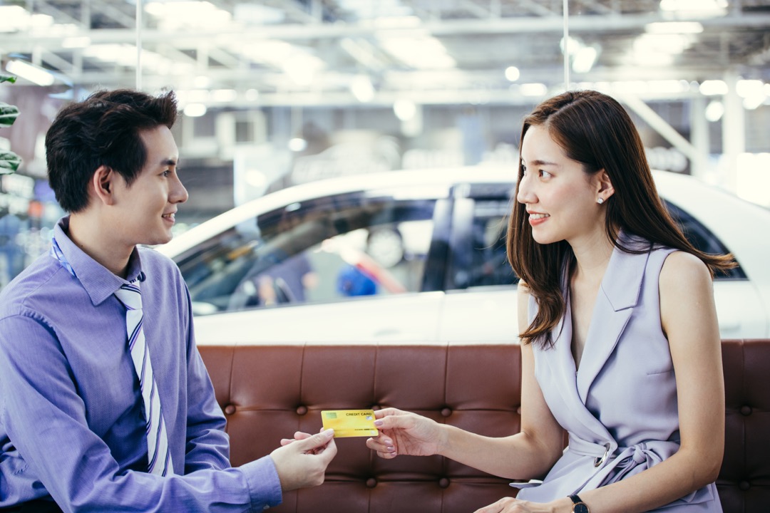 Femme donnant une carte de crédit à l'agent du concessionnaire automobile dans une salle d'exposition automobile.
