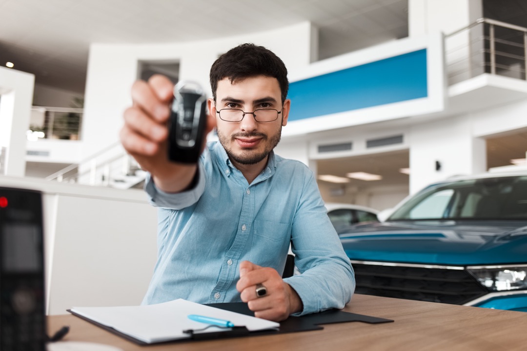 Un vendeur d'automobiles montre une clé de voiture assis à une table dans une salle d'exposition automobile.